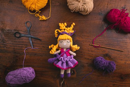 A product photo of a handmade crochet toy doll for kids with its tools and materials