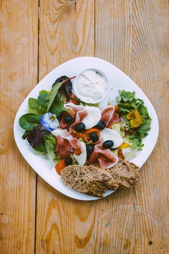 A vertical top view of salad with prosciutto, olives and bread meal on a wooden table