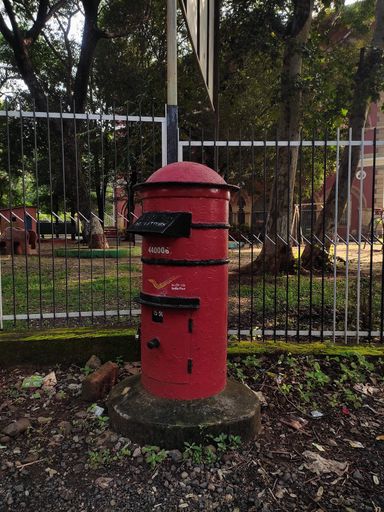 A vertical shot of a post box of the Indian Postal Service near the fence