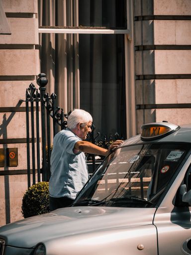 An adult taxi driver leaning on his car on the streets of London, England