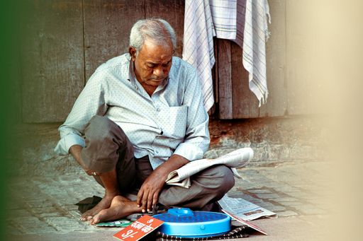 A closeup shot of an old man sitting on the floor reading a newspaper beside a blue weight scale