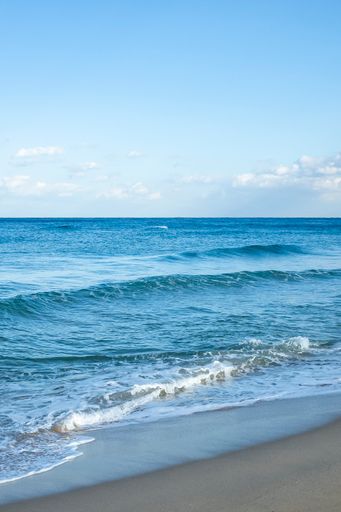 A vertical shot of a sandy coast of a calm sea with few waves