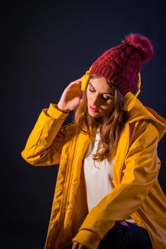 A young Caucasian girl with headphones, yellow jacket and wool hat listening to music in the club