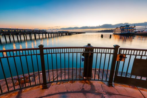 A landscape view of the long bridge and large boat at harbor in San Francisco, California at sunset