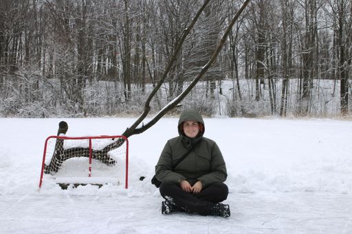A young female in a winter coat sitting on a snowy field near a small net