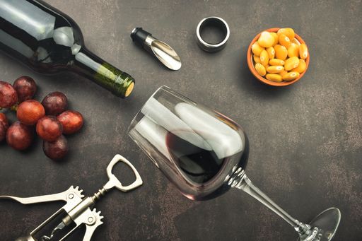 A top view of a red wine glass and bottle on a stone background with a corkscrew, grapes, and lupines