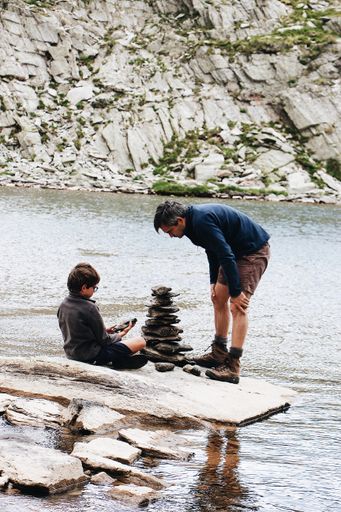 A vertical shot of a man and his son stacking pebbles on the lake shore in France