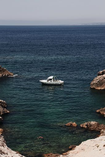A vertical high angle shot of a boat sailing near the rocks in the blue sea