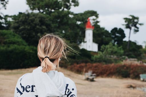 A behind shot of a blonde woman with the lighthouse and trees in the background