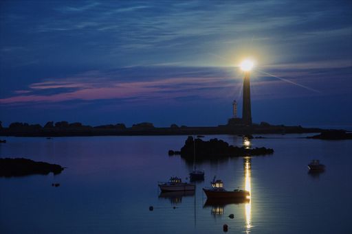 The beautiful view of the lighthouse in the sea with boats in the foreground during sunset