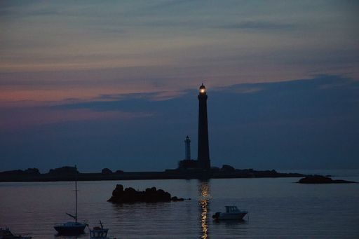 The beautiful view of the lighthouse in the sea with boats in the foreground during sunset