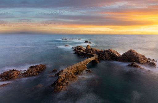 A stunning sunset in Cala canyet with cliffs in the middle in Costa Brava, shot in long exposure