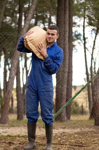 A beautiful shot of smiling young farmer with a sack of feed on his shoulder on his farm and looking at the camera