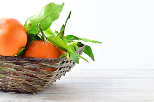 A close-up shot of ripe tangerines with their green leaves in a wicker basket isolated on a white background