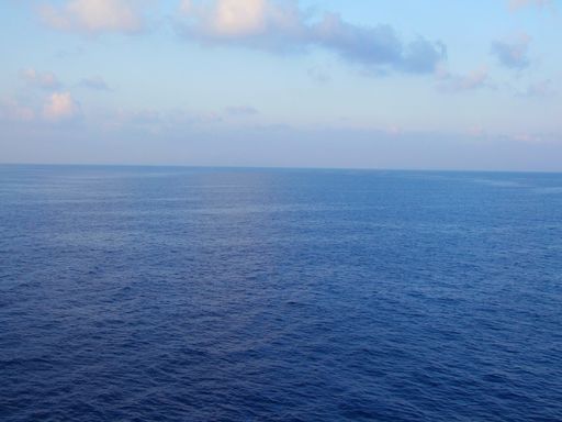 A bird's eye view of a the sea against blue sky with clouds in the early morning