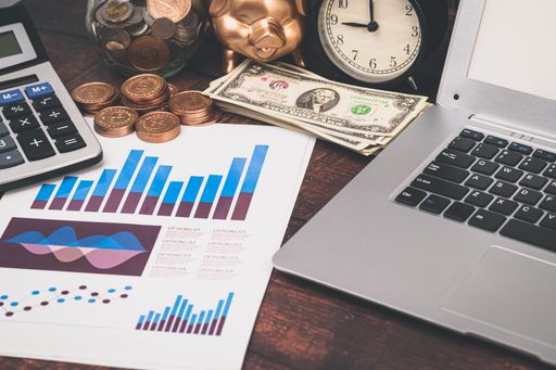 A closeup shot of financial graph documents, golden piggy bank, laptop and coins in a transparent jar