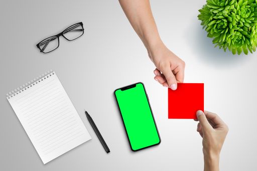 A top shot of a hand passing the empty blank paper to another person with a phone with a green screen display on a blue background.