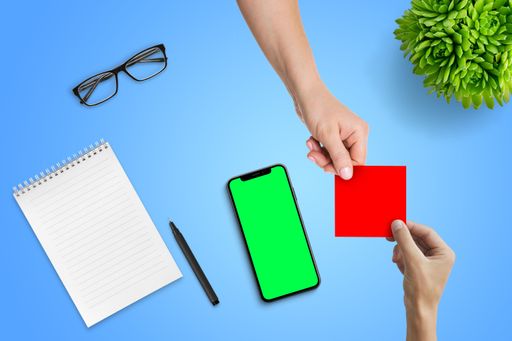 A top shot of a hand passing the empty blank paper to another person with a phone with a green screen display on a blue background.