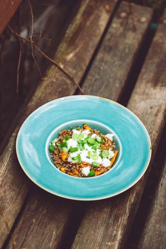 A vertical shot of a vegetable risotto with cream and young onions dish on the plate on the wooden bench.