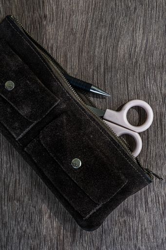 A closeup vertical shot of a suede pencil case with scissors and a pen