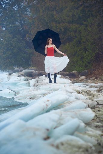 A closeup of a model on ice with umbrella with red top and white skirt
