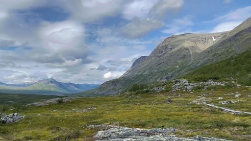 A beautiful scene of a dry green land and mountains under a cloudy blue sky