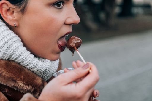 Woman eating festive pastry, winter holiday season food, mini donuts also called fritule or venetian fritole. Pastry covered  with chocolate sauce.