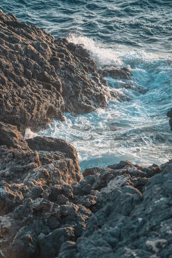 A vertical shot of a body of water near a rocky shore against a light blue sky