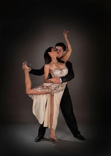 A tango couple of a Latin woman and an Asian man dancing in a black background
