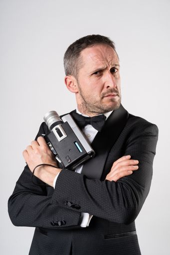 Man in an elegant suit handling a Super 8 camera in classic secret agent pose.