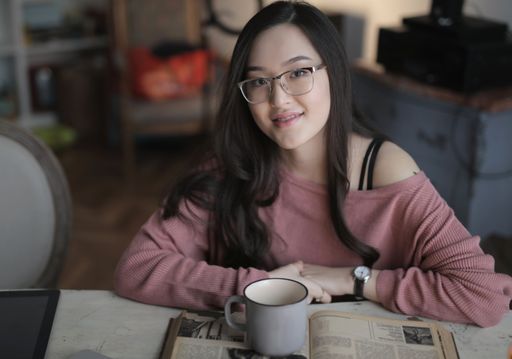 A selective focus shot of pretty female with glasses and pink top sitting in front of her desk