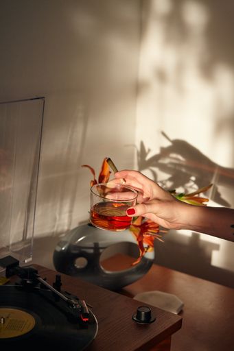 Woman's Hand Holding THC CBD Joint and Whiskey Glass at a record player.