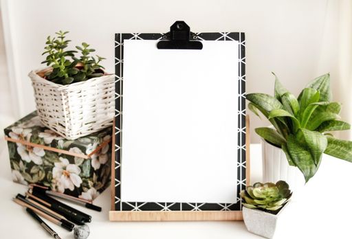 An aesthetic view with a blank paper on board with a copy space near a pile of pens and beautiful houseplants