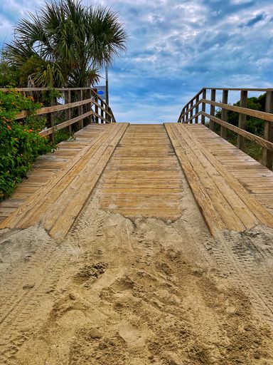 A vertical shot of the wooden path covered with sand.
