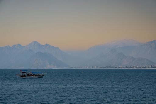 A beautiful view of a small sailboat in the middle of the lake on the mountains background