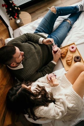 A young couple enjoying snacks and drinks while lounging on a bed