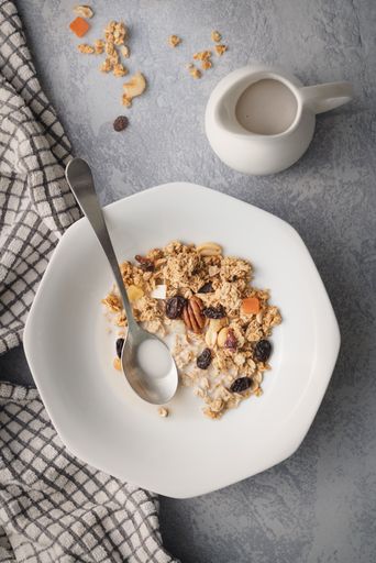A vertical shot of an oaten breakfast with dried and fresh fruits near a milk jug