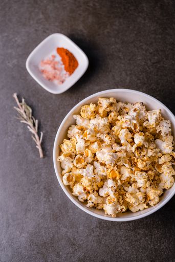 A vertical high angle shot of a popcorn plate near a small plate of spices on a grey surface background