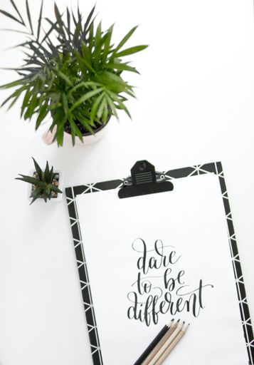 A text on a white paper "dare to be different" on a white background with green plants
