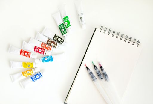 An overhead shot of a blank white paper with painting tools on the white background