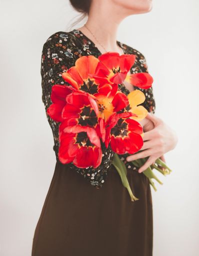A vertical shot of a female holding beautiful colorful tulips standing against a white wall