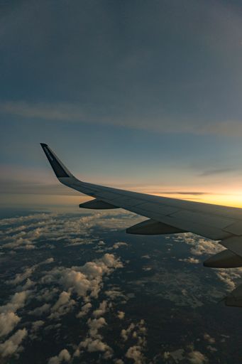 An aerial view from airplane, plane's wing at sunset from right side over clouds horizon