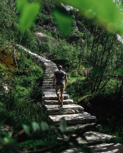 A vertical shot of a man with a t-shirt and shorts walking up the stairs of the green park in spring