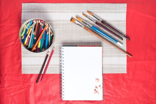 An overhead shot of a can full of pencils with a plain white notebook and brushes