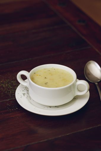 A vertical shot of soup with a spoon and brown table on the background