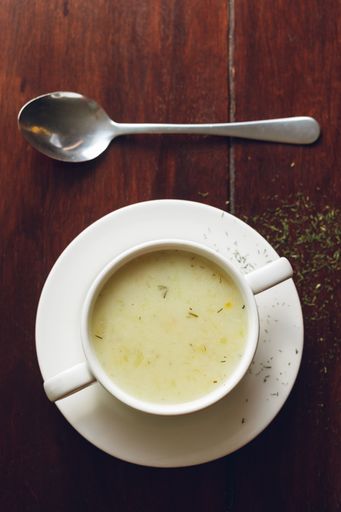 A closeup shot of soup with a spoon and brown table on the background