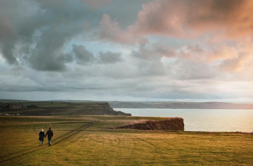 A breathtaking shot of a couple walking holding hands on a cliff at sunset