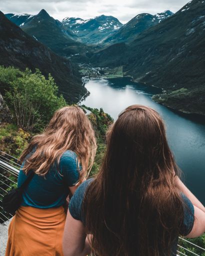 A vertical shot of two girls from behind enjoying the scenery of the blue lakes and huge mountains