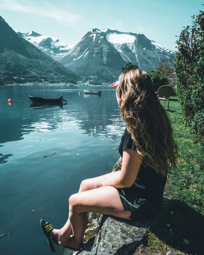 A vertical shot of a girl with long hair resting on the stones and enjoying the view of the lake with