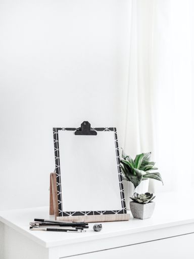 An aesthetic view with a blank paper on board with a copy space near a pile of pens and beautiful houseplants